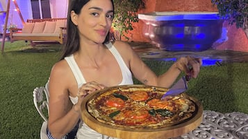 A person seated at an outdoor table with a pizza, surrounded by a decorative metal table with intricate patterns.