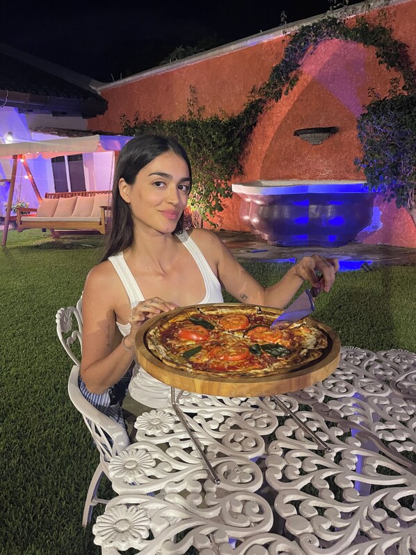 A person seated at an outdoor table with a pizza, surrounded by a decorative metal table with intricate patterns.