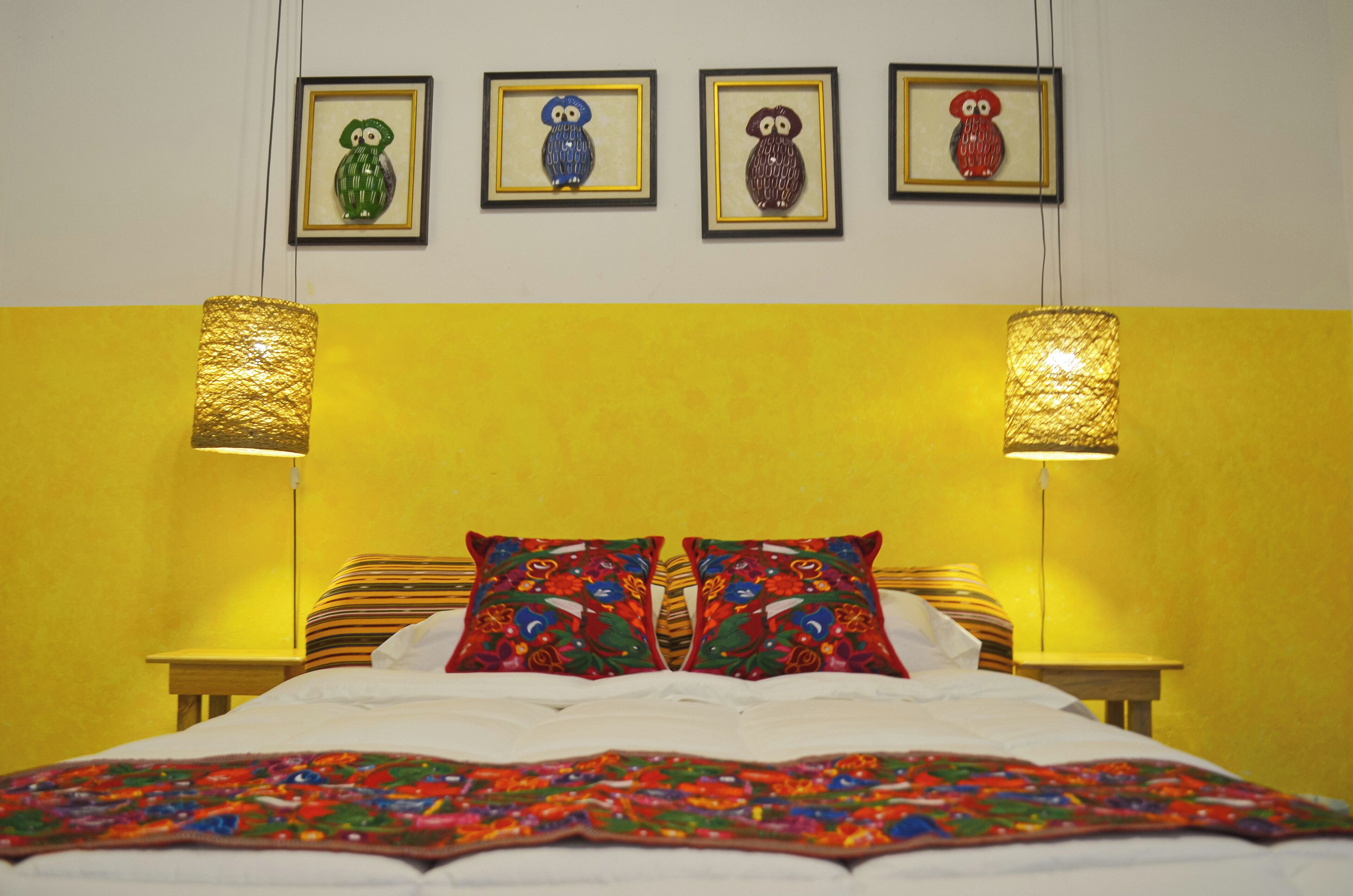 Una cama con almohadas coloridas y una colcha estampada, una obra de arte enmarcada en la pared y dos lámparas a cada lado.
