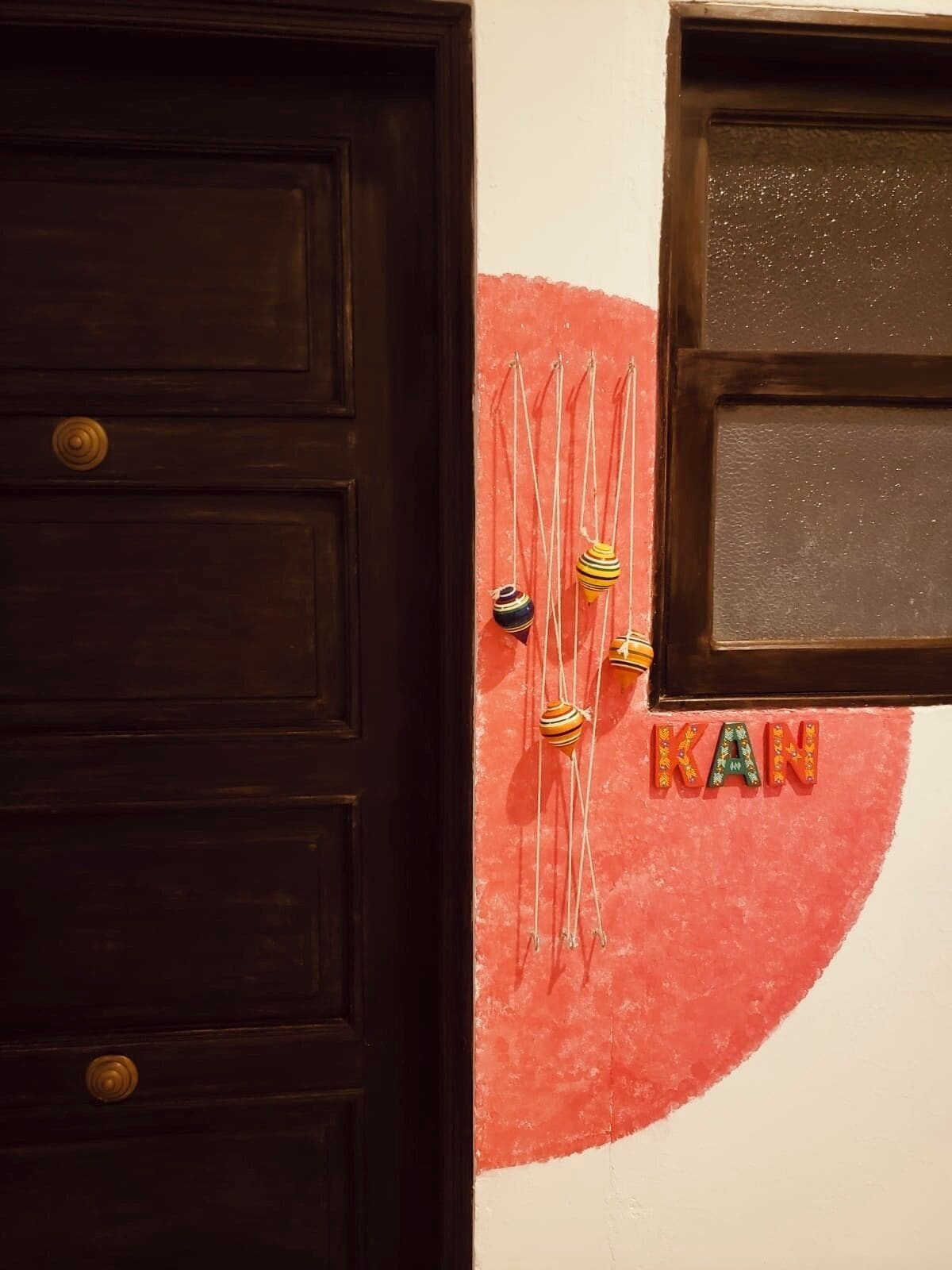 Una puerta de madera oscura con herrajes de latón y una ventana con marco texturizado.