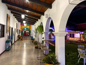 Un pasillo con piso de baldosas, un mural colorido y una zona de estar con sillas y mesas.