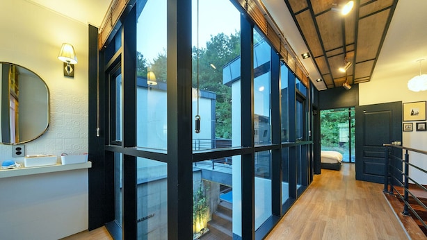 A modern hotel room with large glass doors leading to a balcony, a wooden floor, and a bed with a view. - Ulsan Byeoldam Eunchae Pool Villa (Ulsan)