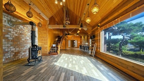 A spacious interior with a wooden floor, a fireplace, a staircase, and a large window offering a view of trees. - Ulsan Byeoldam Eunchae Pool Villa (Ulsan)