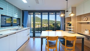 A modern kitchen with a large dining table, wooden chairs, and a view of hills through the glass doors. - Ulsan Byeoldam Eunchae Pool Villa (Ulsan)