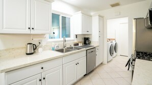 A modern kitchen with white cabinets, a stainless steel coffee maker, a dishwasher, and a built-in stove.