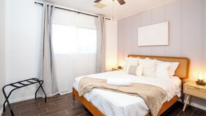 A neatly made bed with a wooden headboard, a bedside table with a lamp, and a ceiling fan.