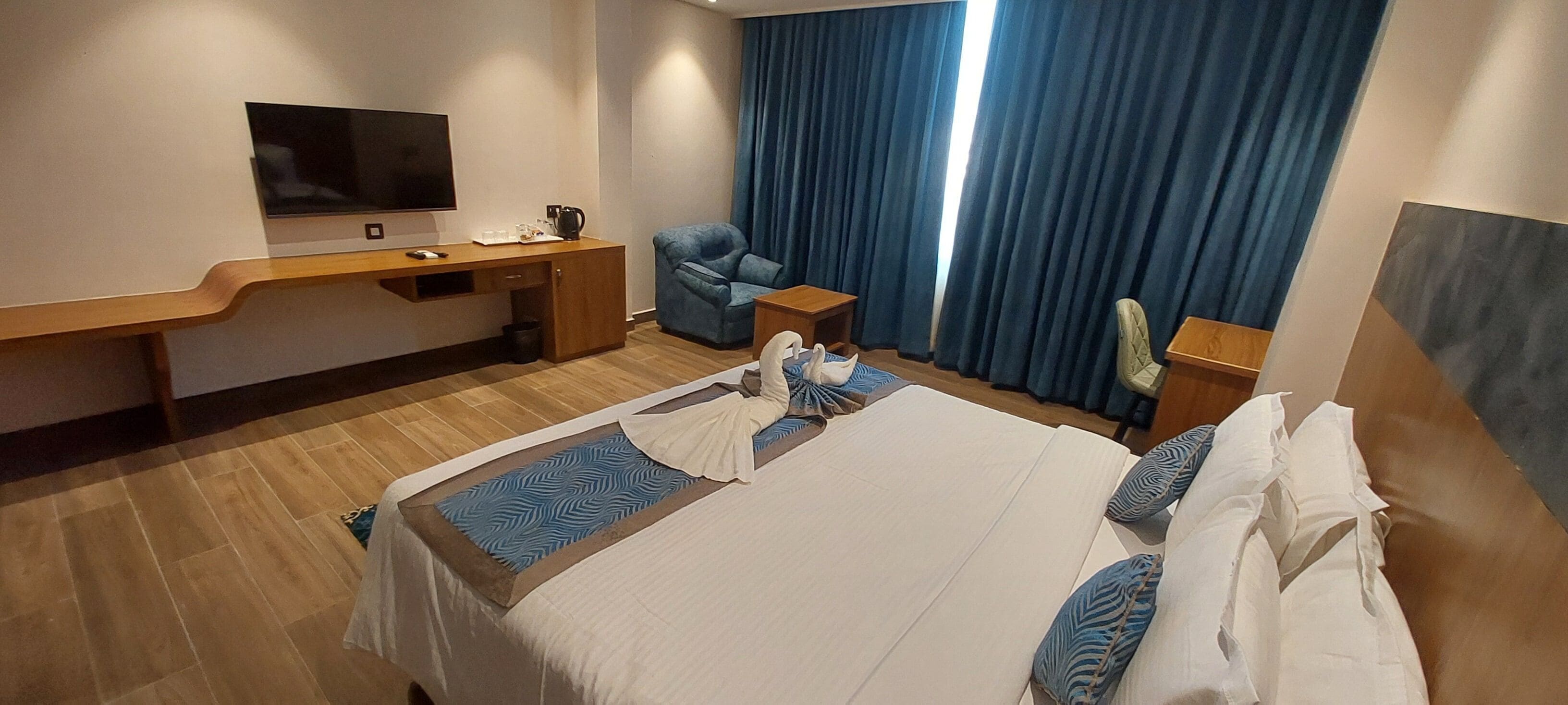Camera d'albergo con un letto, una scrivania, una sedia, una televisione e una finestra con tende.