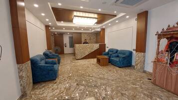 Un vestíbulo de hotel con una recepción, sillones azules, piso de mármol y una araña.
