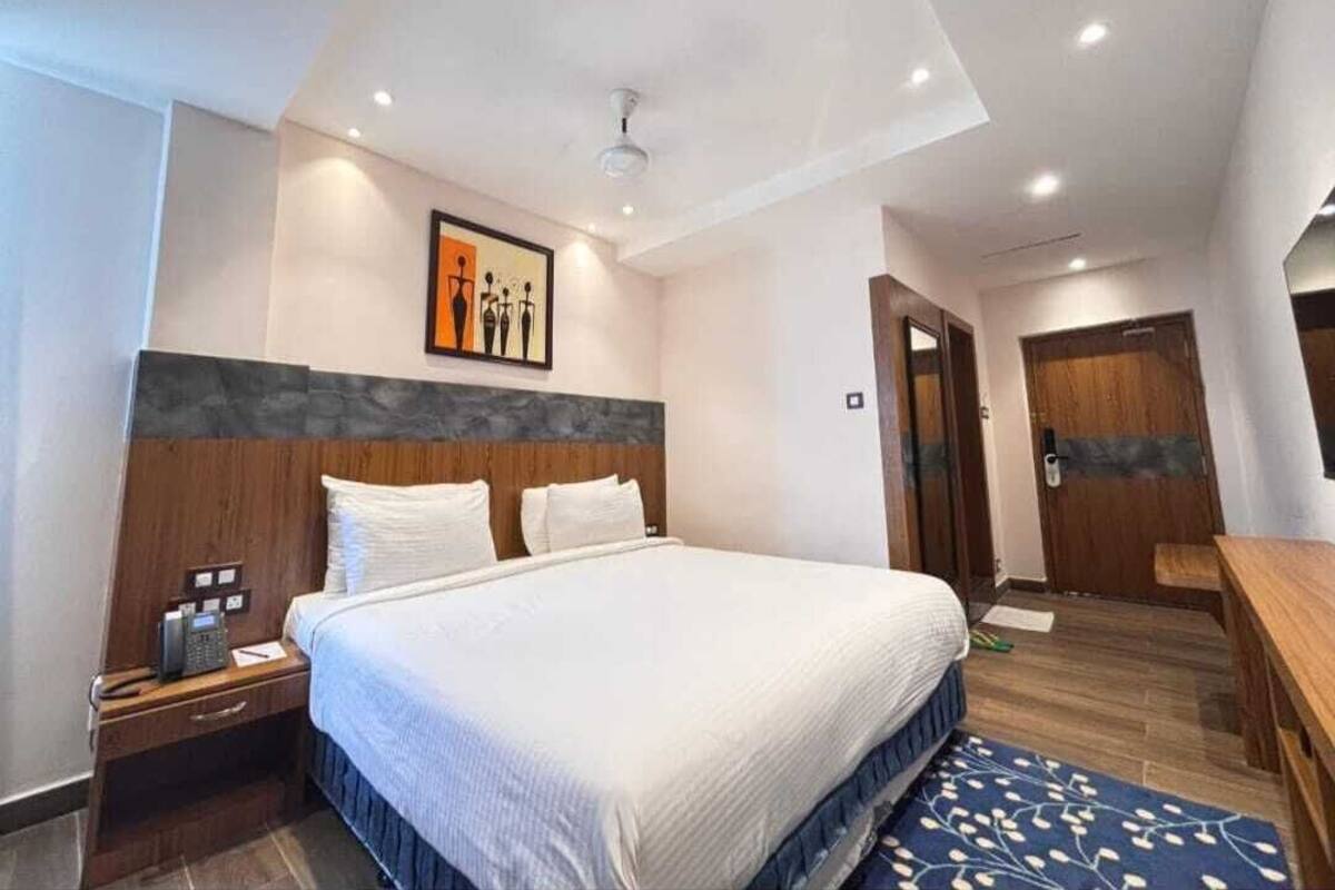 A modern hotel room with a large bed, a wooden headboard, a desk, and a painting on the wall.