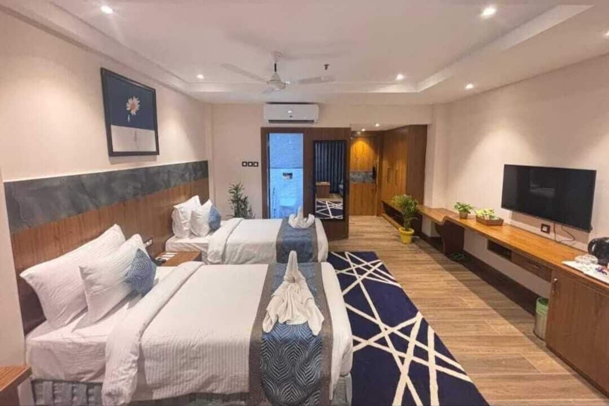 A hotel room with two beds, a TV, a desk, and a bathroom visible through an open door.