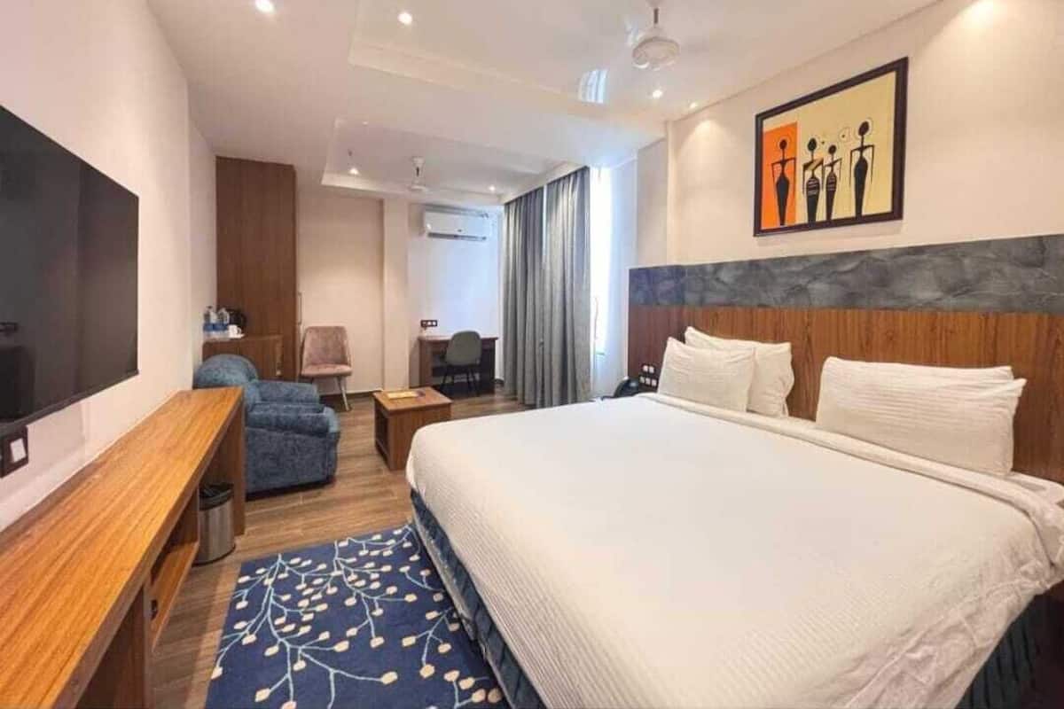 A modern hotel room with a large bed, a desk, a chair, and a TV.