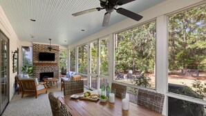 A spacious patio with a brick fireplace, wicker furniture, and a dining table set with food and candles. - Wilson Cottages, Walk to Tennis & Pickleball, and Restaurants (Bluffton)