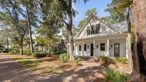 A white house with a front porch, surrounded by trees and a brick pathway. - Wilson Cottages, Walk to Tennis & Pickleball, and Restaurants (Bluffton)