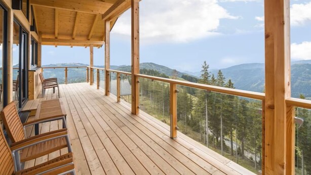 Una terraza de madera con barandilla, con vista a un paisaje montañoso.