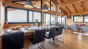 Interior de madera con mesa de comedor preparada para cuatro comensales, ventanas amplias y chimenea.