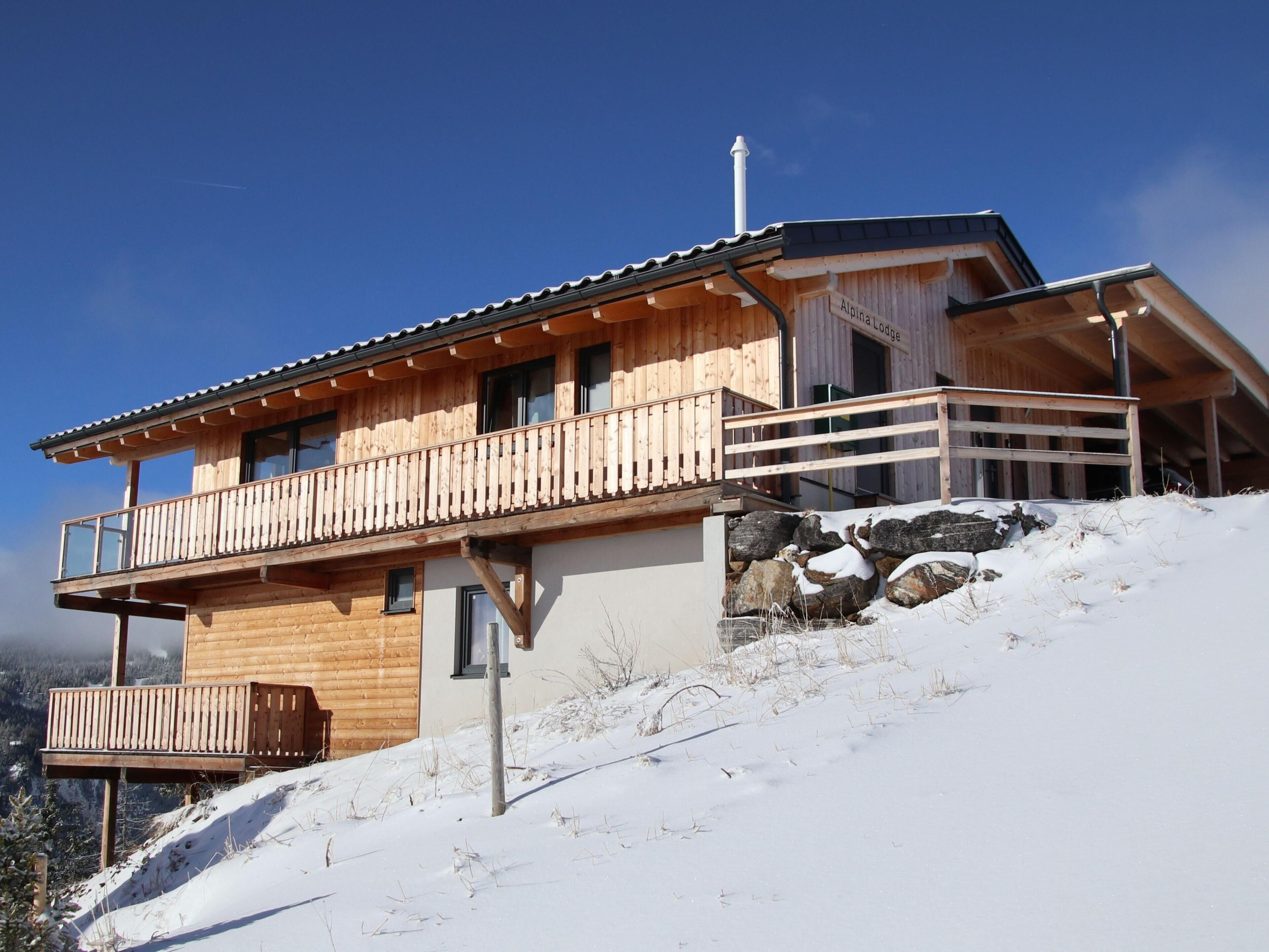 A wooden chalet with a balcony, a stone foundation, and a clear sky.