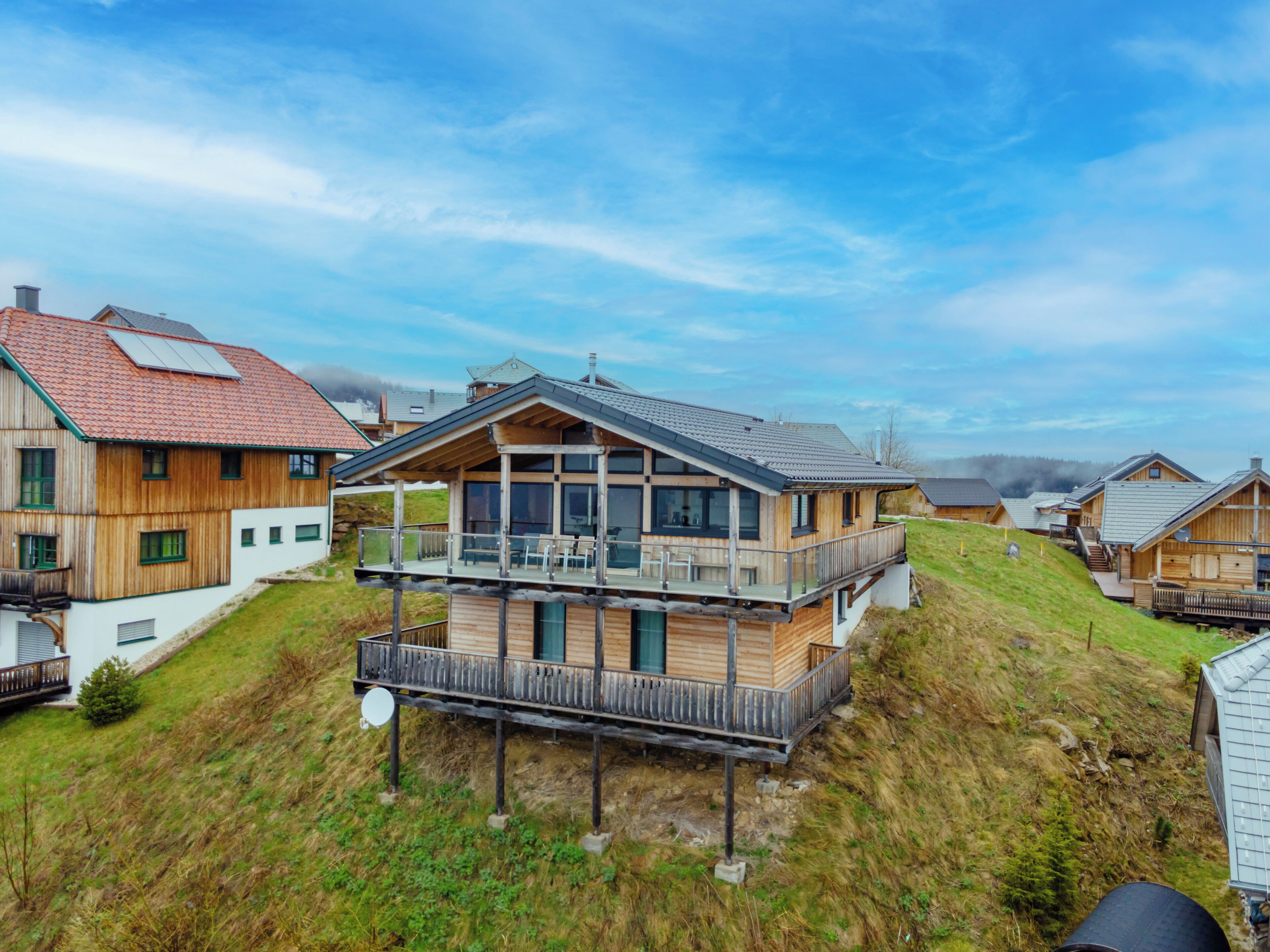 Uma casa moderna de madeira com varanda, cercada por colinas gramadas.