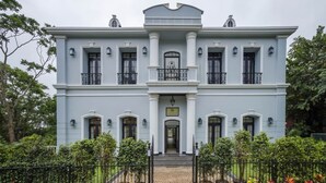 A large, two-story building with a symmetrical facade, multiple windows, and a central entrance with a decorative gate. - Luxury 3BR Duplex With Pool in Goa s Beverly Hills (Assagao)
