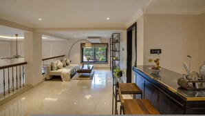 A spacious living area with a sofa, coffee table, and a dining table. A kitchen area with a counter and sink is visible. - Luxury 3BR Duplex With Pool in Goa s Beverly Hills (Assagao)
