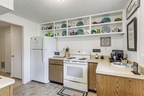 Una cocina con electrodomésticos blancos, gabinetes de madera y platos decorativos en estantes.