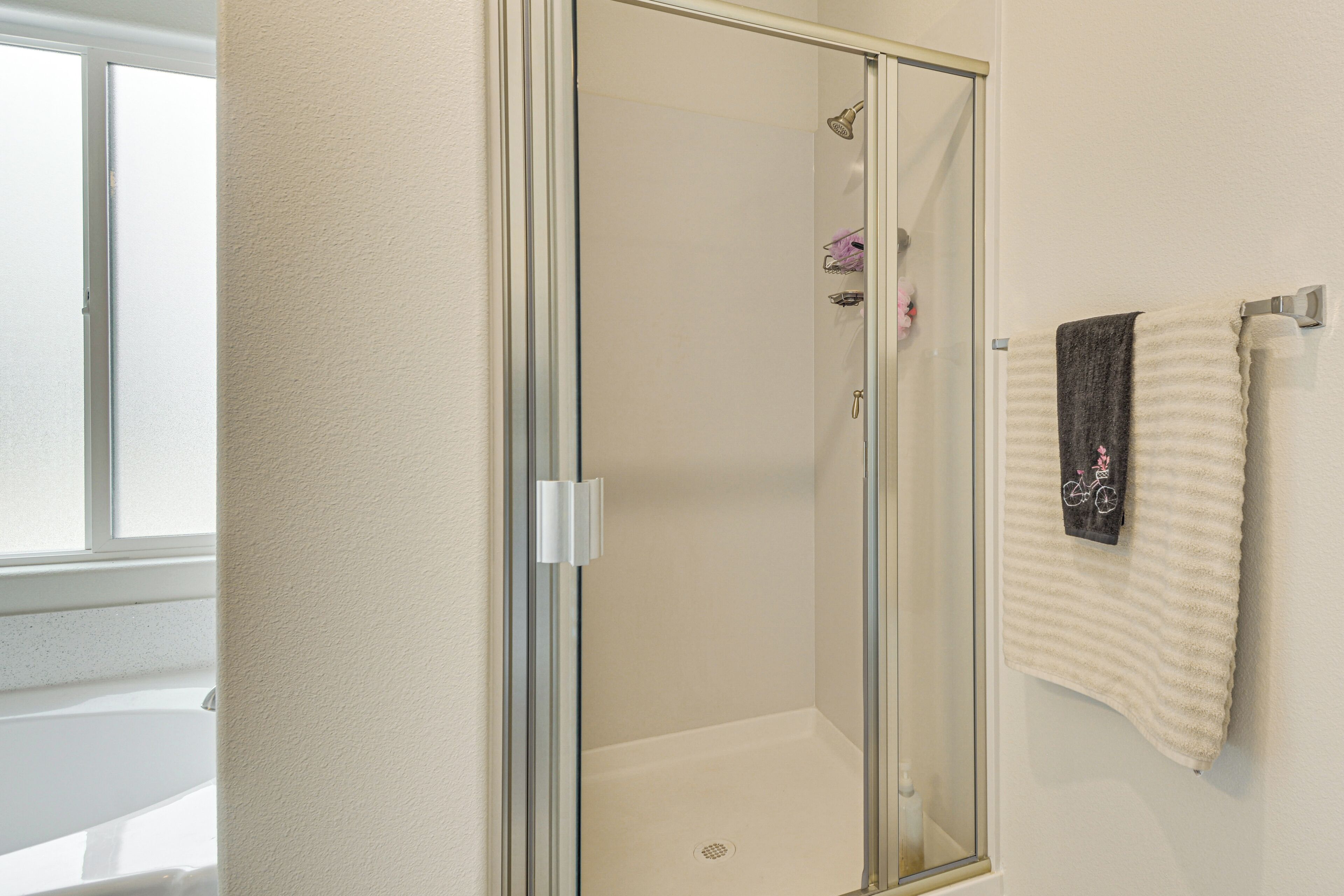 Une douche fermée par des parois de verre, avec une serviette blanche accrochée au mur.