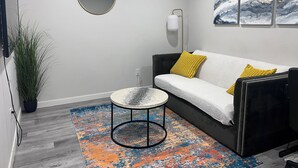 A modern living room with a sofa, a round table, a potted plant, and a colorful rug. - Cozy basement suite in Elerslie . (Edmonton)