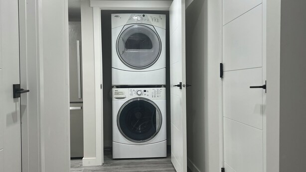 A laundry room with two stacked front-loading washing machines, a vent, and a wooden floor. - Cozy basement suite in Elerslie . (Edmonton)