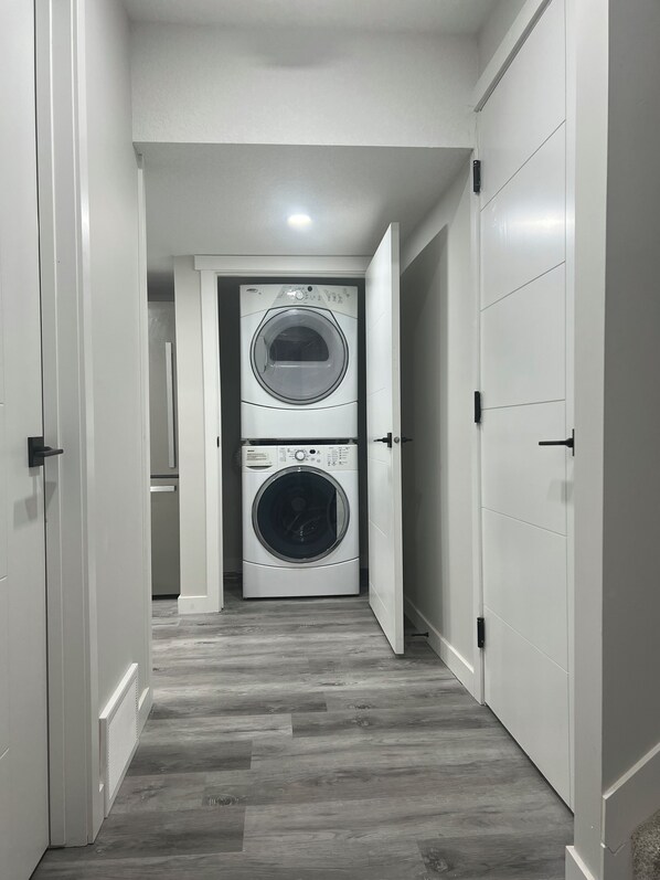 A laundry room with two stacked front-loading washing machines, a vent, and a wooden floor.