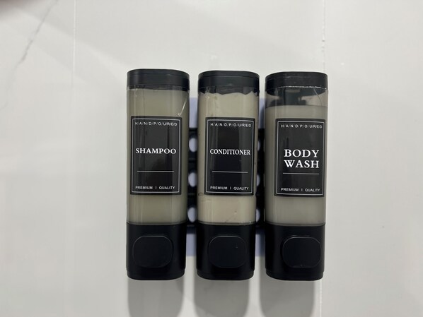 Trois bouteilles de shampoing, d’après-shampoing et de gel douche, disposées côte à côte sur une surface blanche.