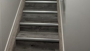 A staircase with wooden steps and a handrail, leading to a white door. There are two wall-mounted thermostats on the right side. - Cozy basement suite in Elerslie . (Edmonton)