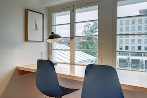 A room with a large window, a desk, two chairs, and a pendant lamp.