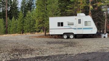 A white RV parked on a gravel surface with a forest in the background.