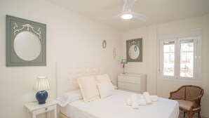 Ein Schlafzimmer mit Bett, Nachttisch, Lampe, Kommode, Stuhl und Deckenventilator.