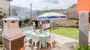 An outdoor patio with a table set for dining, a barbecue grill, and a large umbrella providing shade.