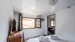A bedroom with a bed, a wooden dresser, a mirror, and a window with a view of buildings outside.