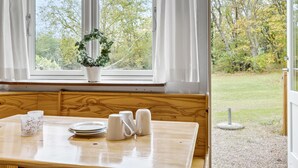 Un banco de madera con una mesa delantera, una planta en maceta en el alféizar de la ventana y vistas a un área verde exterior.