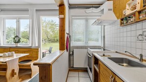 Cocina compacta con armarios de madera, horno integrado y un amplio ventanal con persianas.
