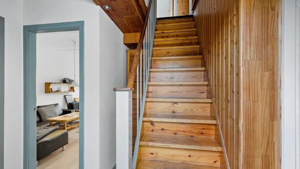 Una escalera de madera que sube a un segundo piso, con una sala de estar visible en la planta baja.
