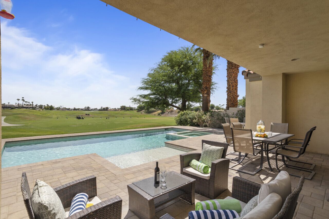 A poolside area with outdoor furniture, a view of a golf course, and a clear sky.