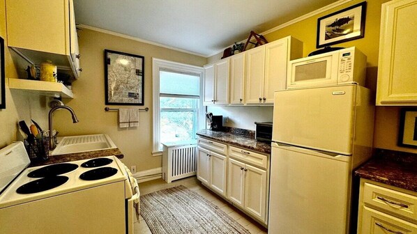 A kitchen with white cabinets, a stove, a microwave, and a refrigerator. - Commanders Cabin, quaint apt steps to downtown (Camden)