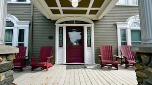 Eine Veranda mit roter Tür und Steinsäulen, umgeben von roten Adirondack-Stühlen.