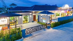 A modern hotel with a covered outdoor seating area, large windows, and a well-lit entrance. - Baandomedoodao Pool Villa Cha-Am (Cha-am)