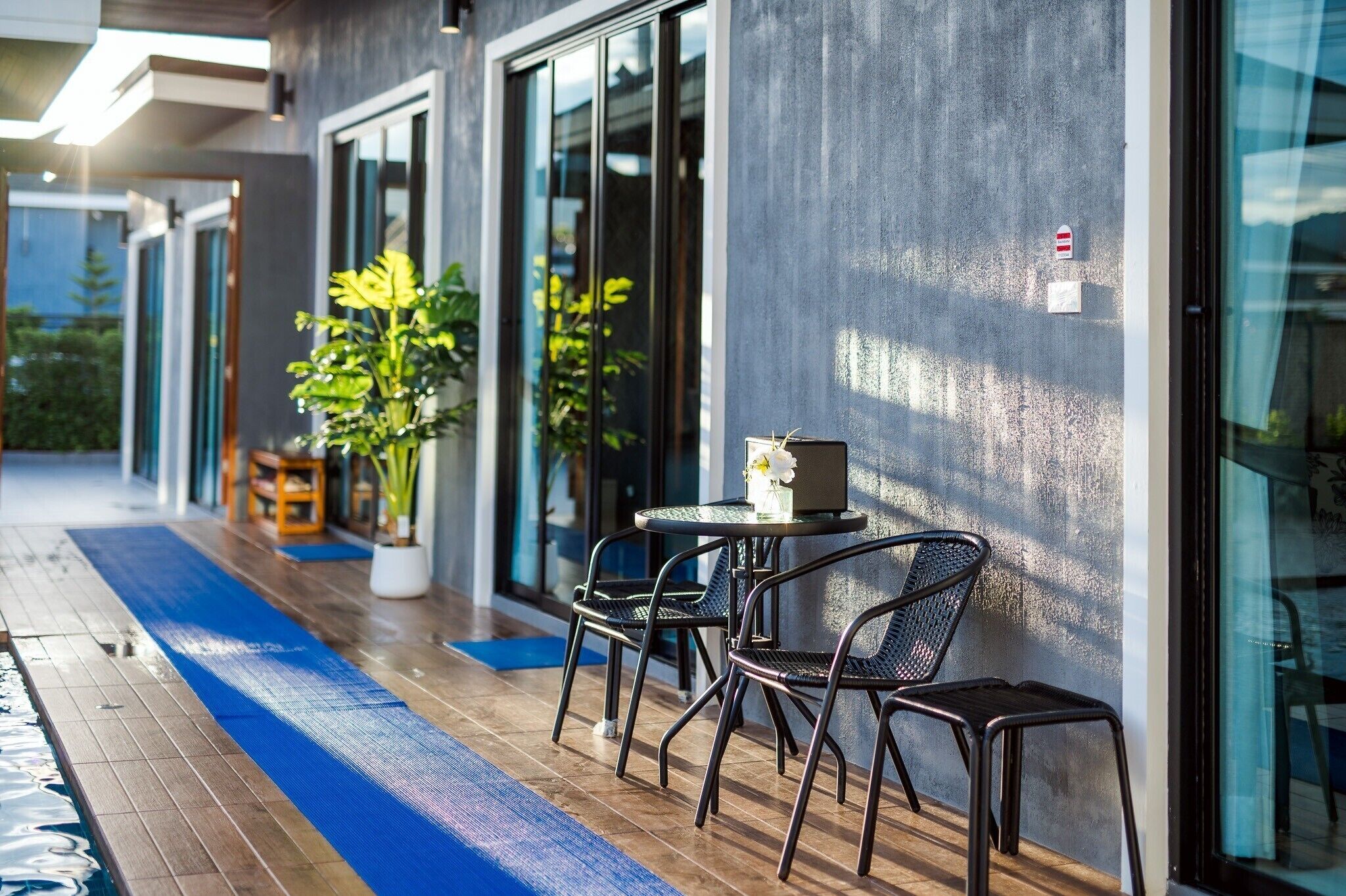 An outdoor seating area with a blue mat, metal chairs, and a table with a vase of flowers.