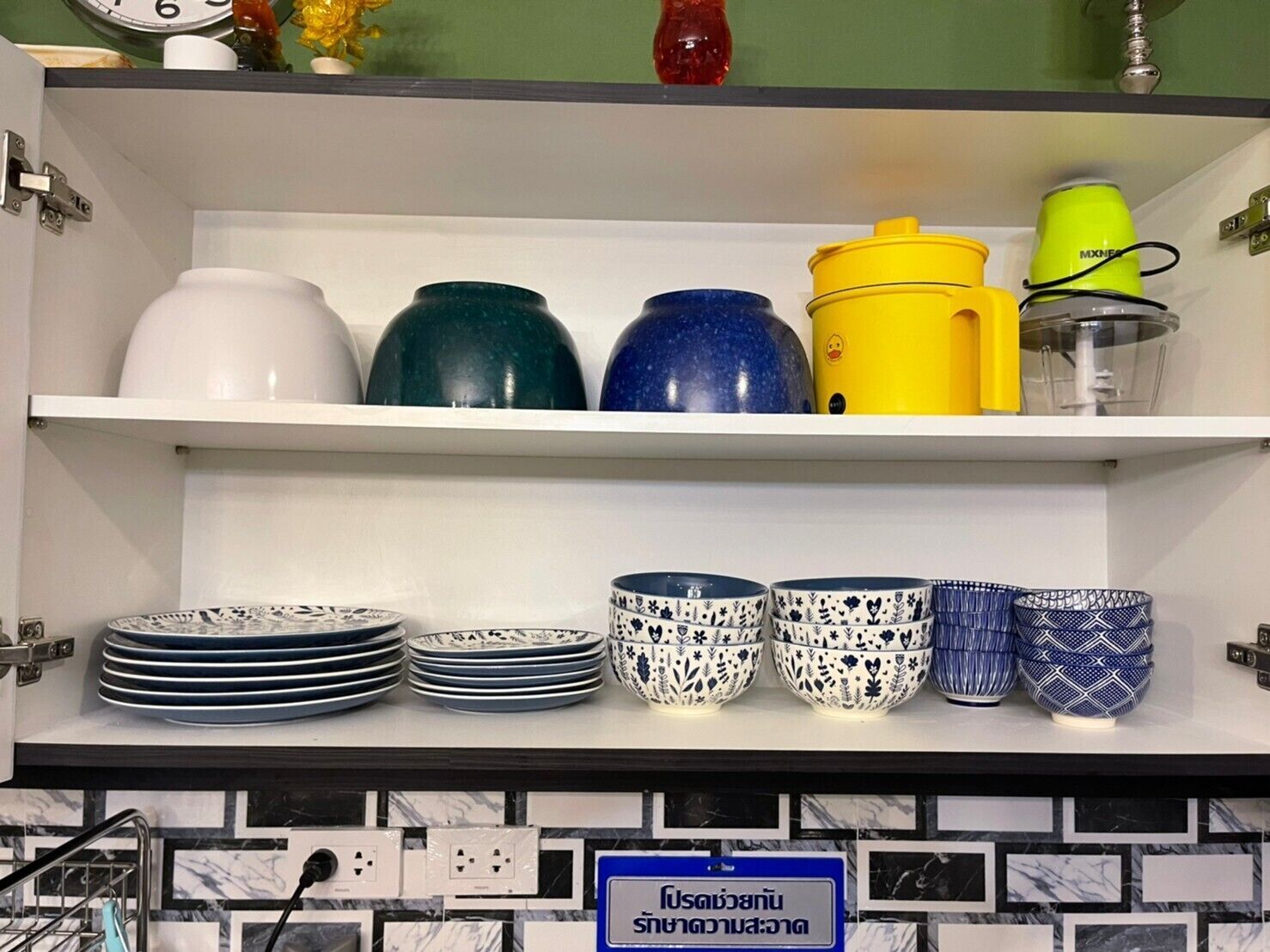 En kökshylla med olika köksredskap, inklusive tallrikar, skålar och en vattenkokare.
