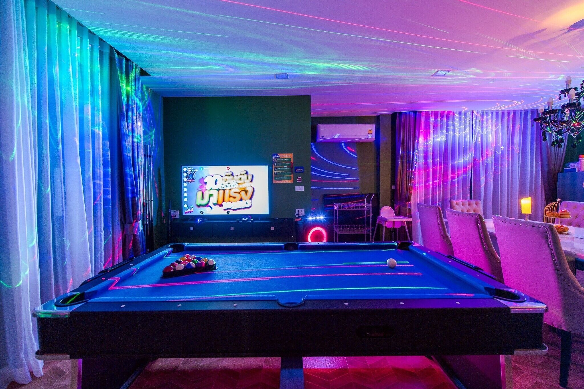 A pool table with neon lights, a television screen, and a dining area with chairs and a table.
