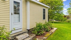 A house with a white door, a small window, and a stone pathway leading to the front. - Puffins Perch, romantic waterfront Maine cottage (Saint George)