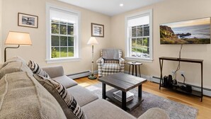A living room with a sofa, armchair, coffee table, lamp, TV, and a view of the outdoors. - Puffins Perch, romantic waterfront Maine cottage (Saint George)