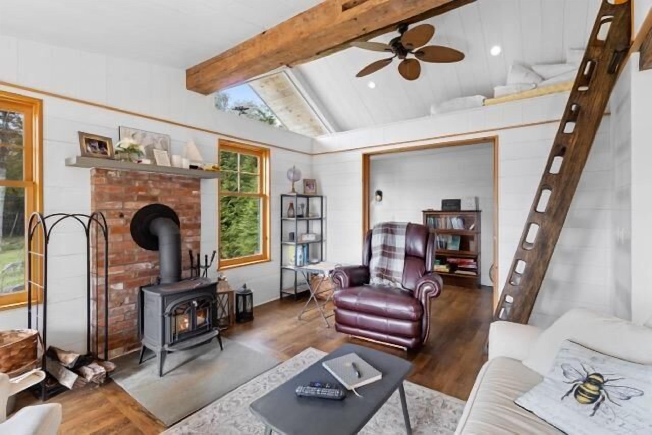 A cozy living room with a fireplace, leather armchair, and a loft bedroom with a ladder.