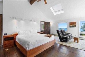 A bedroom with a large bed, a chair, a desk, and a window with a view.