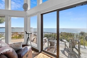 A room with a large sliding glass door leading to an outdoor deck with chairs and a view of the water. - Clark Point Cottage, ocean access, panoramic views (Saint George)